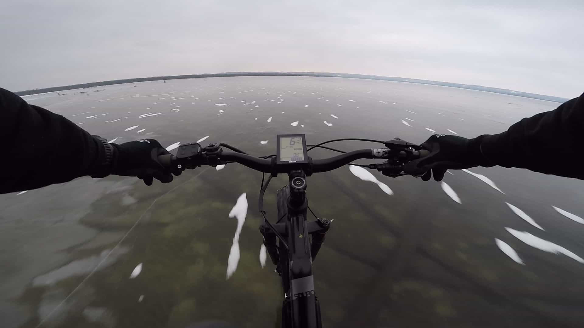 Ciclista atravessa lago congelado transparente